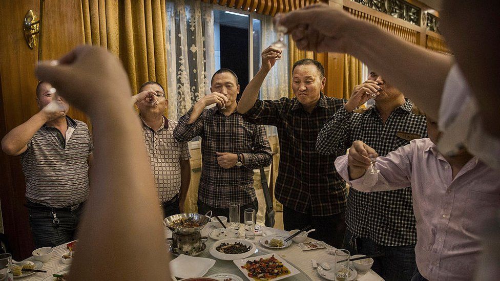 Китайские мужчины тосты друг за друга и пьют мутаи, самое известное вино под названием байцзю