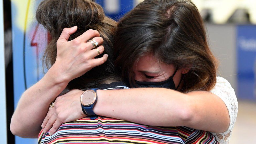 Две женщины обнимают друг друга, когда они воссоединяются в аэропорту Новой Зеландии