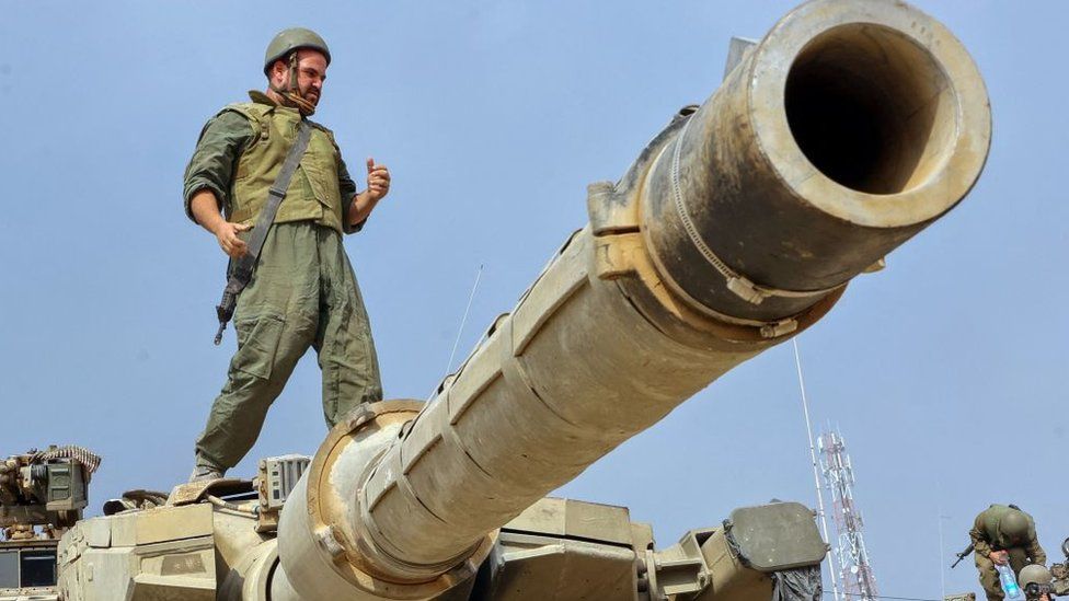 An Israeli serviceman stands atop a tank