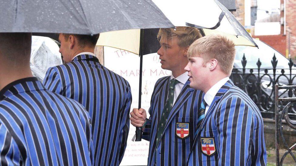 A gorup of four boys in school uniform standing under an umbrella