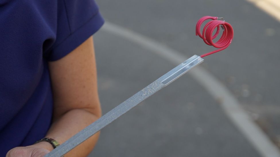 A zinc anode being held. It is a thin piece of metal with red wiring at the top.