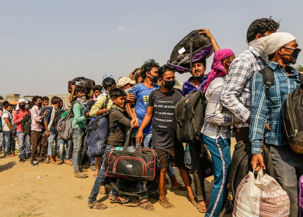 Migrant workers with their families queue up waiting to board buses back home.