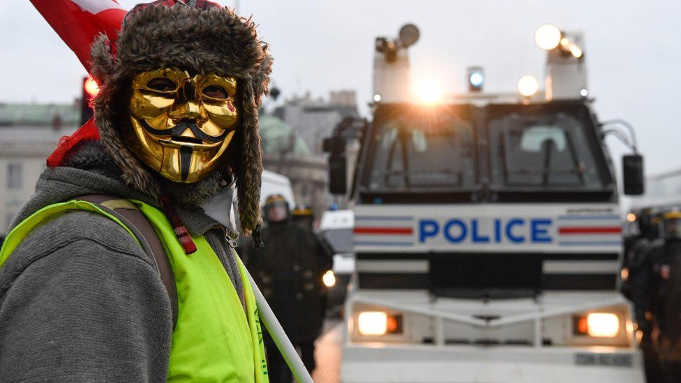 A masked protestor stands in front of a police vehicle in Paris on 5 January 2019, during a rally by yellow vest "Gilets Jaunes" anti-government protesters