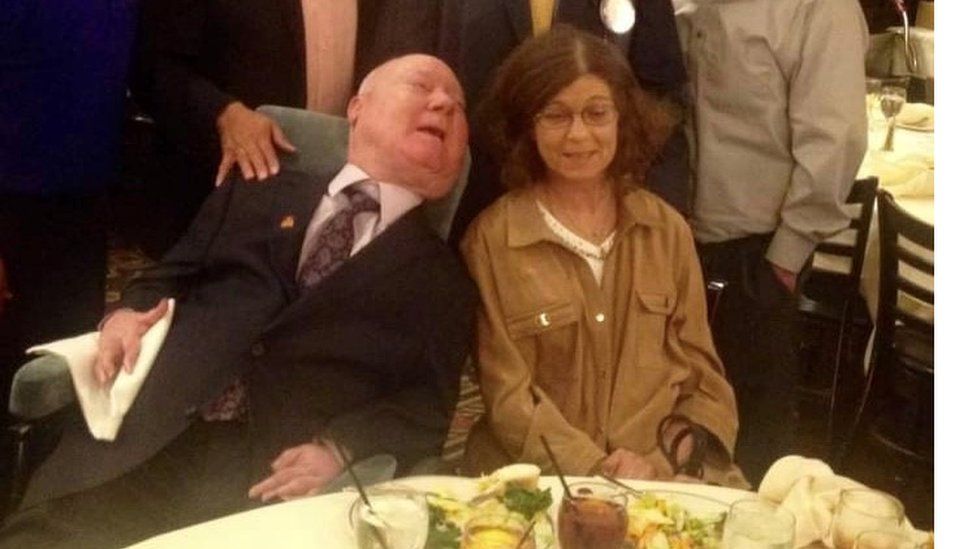 Paul sitting in his wheelchair next to Kathy Gaines at a dinner table