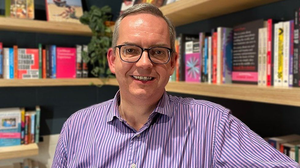 John facing camera in front of bookcase