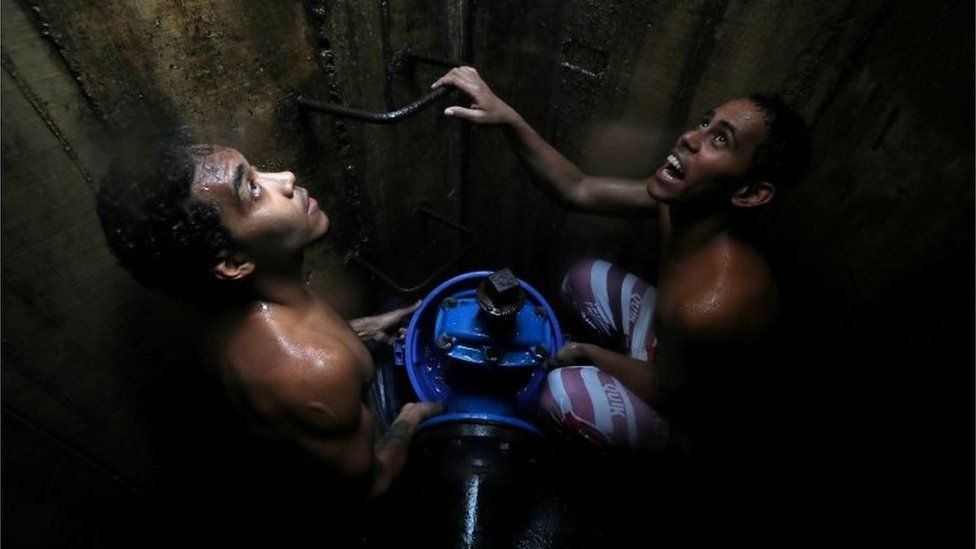 Locals collect water from an underground water main pipeline in Caracas, Venezuela March 12, 2019.