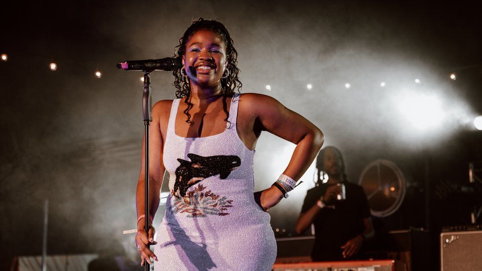 Debbie performs onstage, she's wearing a sequin lilac mini formal  with a slayer  whale print. She's smiling, her hairsbreadth  is pulled backmost  disconnected  her face, brushed  curls remainder  connected  her shoulders.