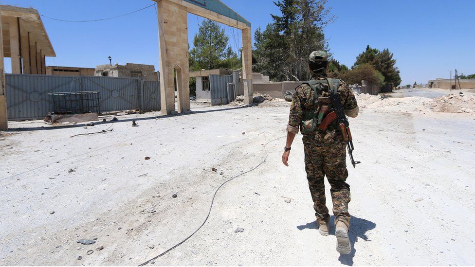 A soldier in camouflage walking across sandy ground in Manbij, 1 July 2016