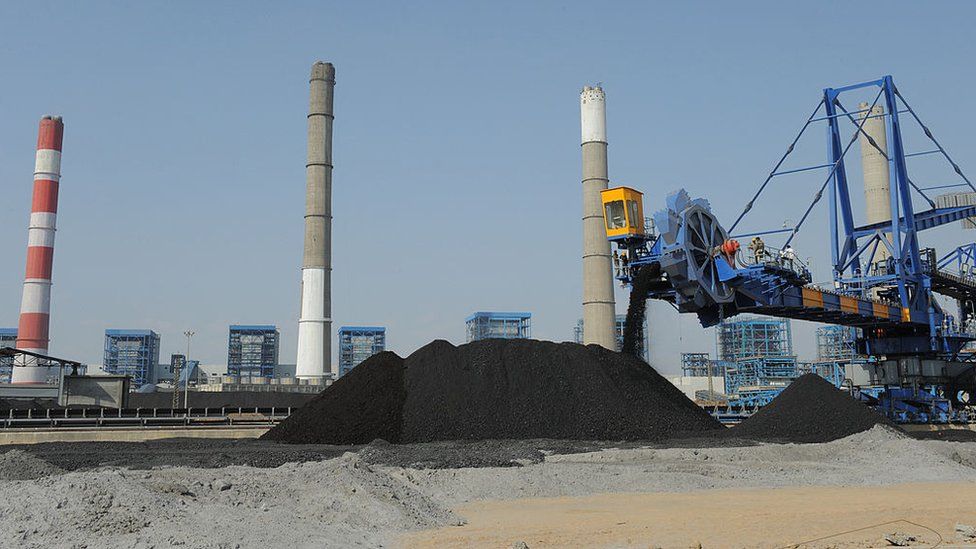 Workers use heavy machinery to sift through coal at the Adani Power company thermal power plant at Mundra