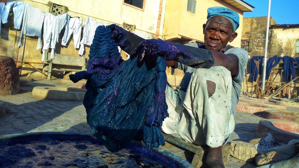 Местный красильщик Баба Мухаммед погружает ткань в краску в Кано, Нигерия