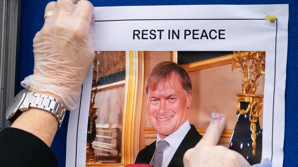 Person puts poster tribute to David Amess up
