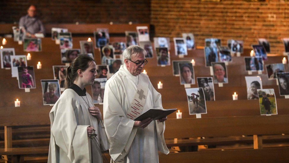 Deacon Bernd Malecki and server Anna hold an Easter service in front of portraits of believers at the St. Barbara church in Oberhausen, western Germany.