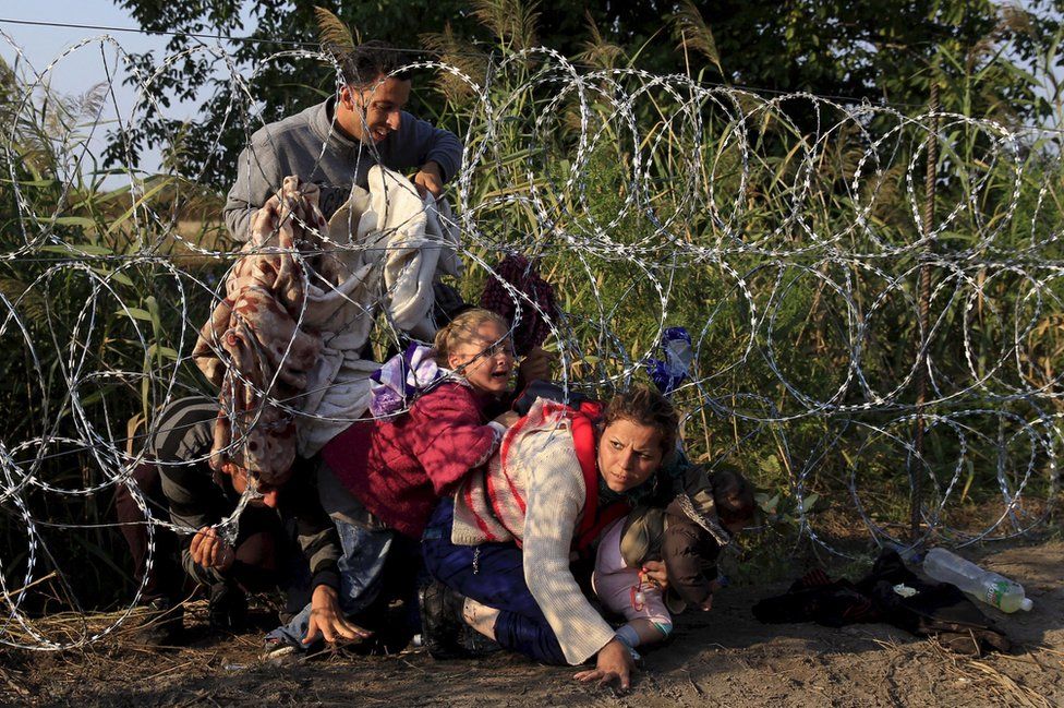 Syrian migrants cross under a fence into Hungary at the border with Serbia, near Roszke, 27 August 2015