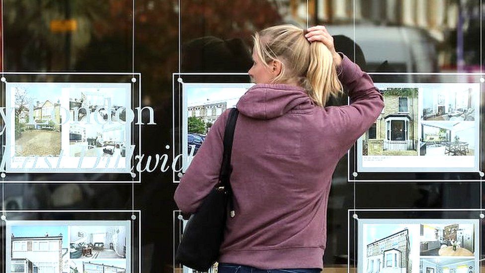 Woman looking at houses for sale in estate agent window