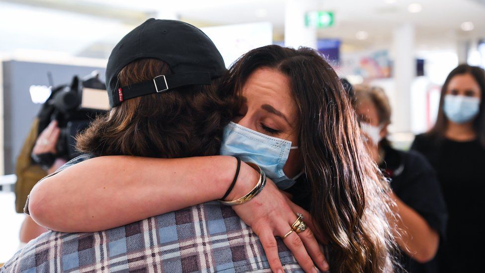 A woman wears a facemask as she hugs her loved one after arriving into the international arrivals area at Sydney's Kingsford Smith Airport from landing on Air New Zealand flight number NZ103 from Auckland on October 16, 2020 in Sydney, Australia.
