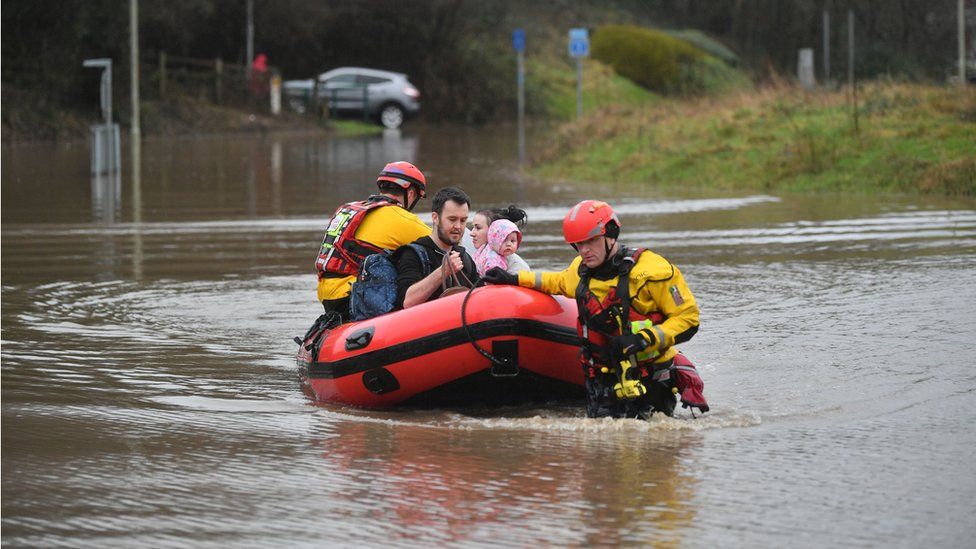 A family in a boat is helped by emergency workers in Nantgarw, Wales