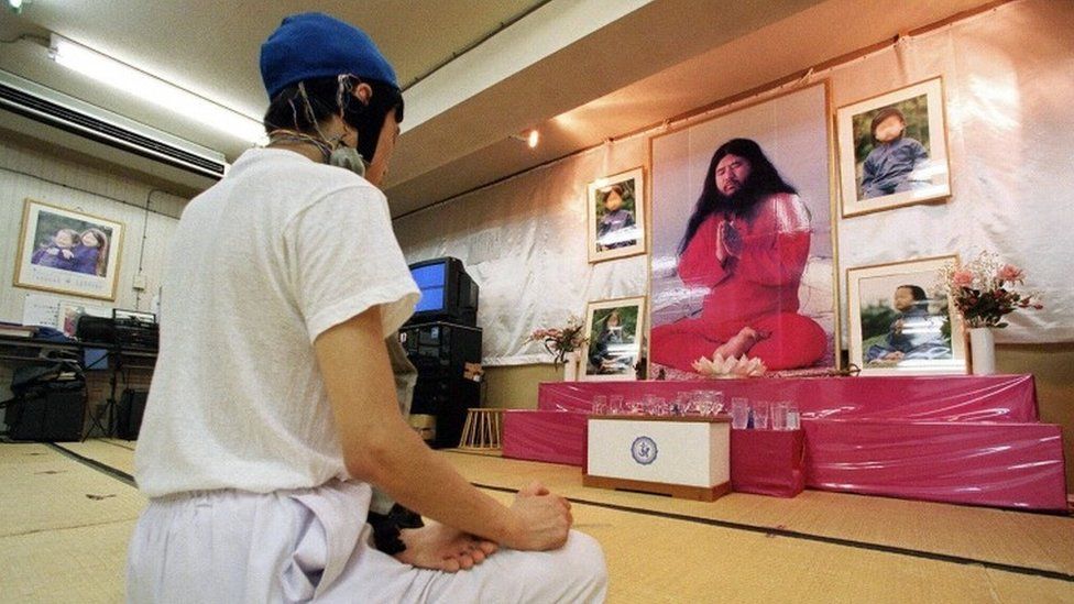 Follower meditating in front of portraits of Aum Supreme Truth guru Shoko Asahara (1999)