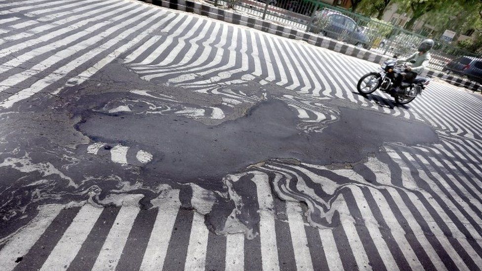 A man in India rides a bike along a melted road
