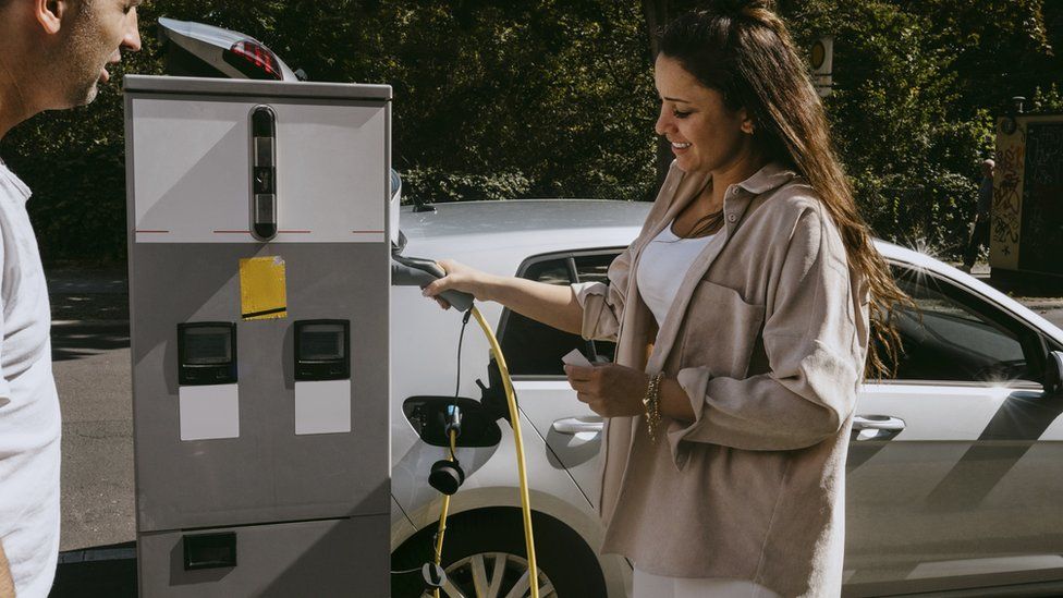 Smiling mother holding electric plug standing by father at gas station