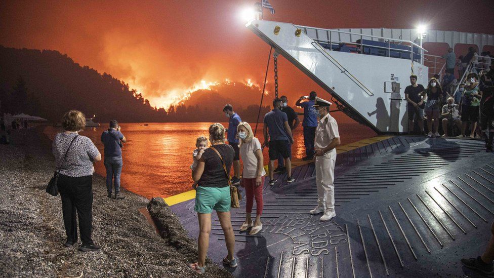 People waiting to be evacuated from the Greek island of Evia by ship with wildfires raging in the background