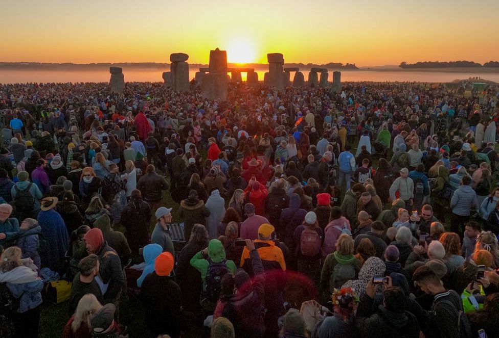 Visitors watch the sunrise at Stonehenge, on June 21, 2024 in Wiltshire, England, 21 June 2024. A crowd stands in the foregorund looking towards the sun which is visible between stones in the background