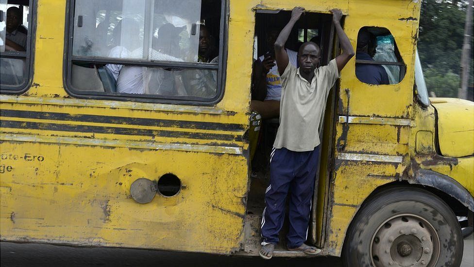 A man looks look out from the open door of a yellow bus in Lagos, Nigeria