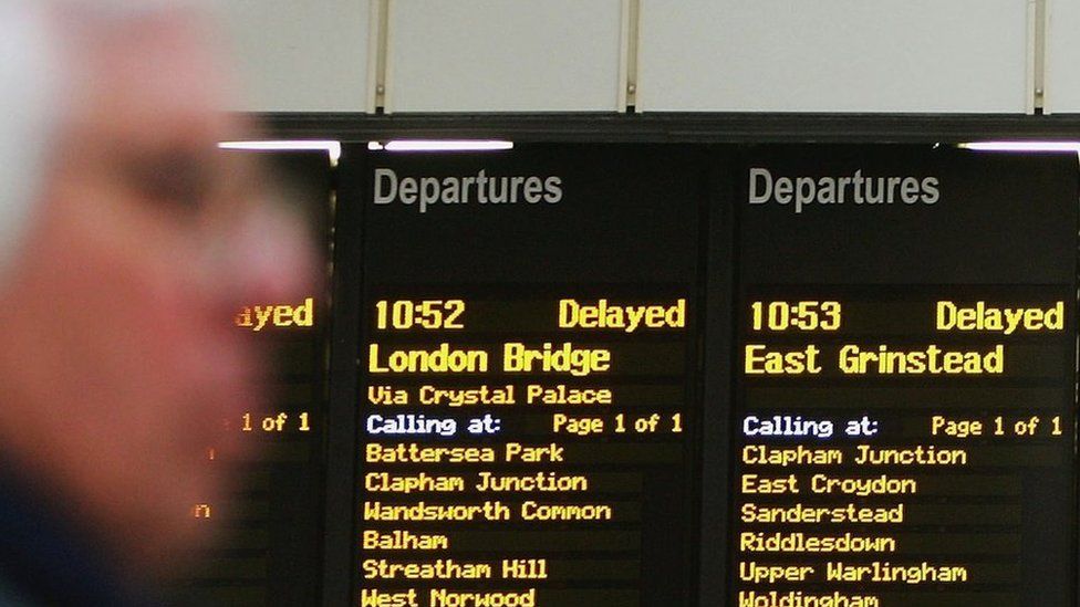 A man in the foreground of a train departures board