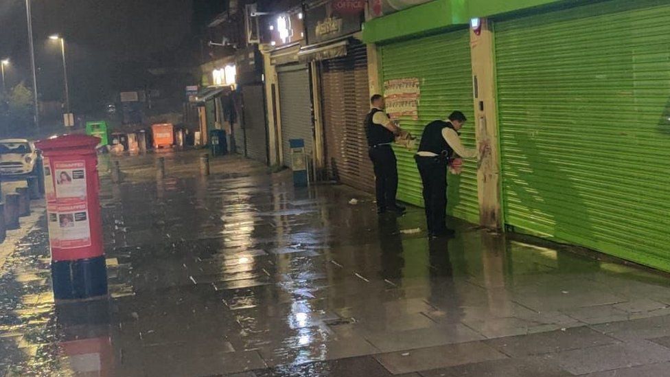 Two officers removing hostage posters from business shutters in Edgware