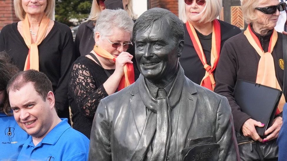 Close-up of Sir David Amess' statue surrounded by people in Southend