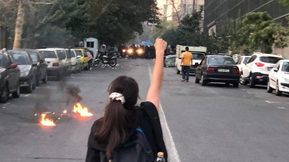 A young woman without a headscarf raises a fist at a protest in Iran sparked by the death of Mahsa Amini