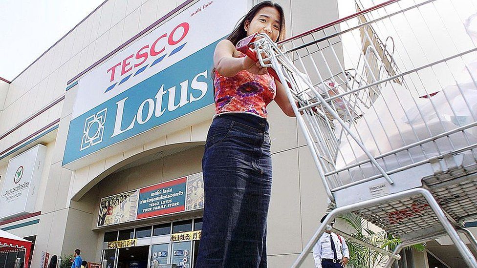 A Thai woman pushes a trolley past the entrance of the Thai outlets of British supermaket chain Tesco Lotus in Bangkok