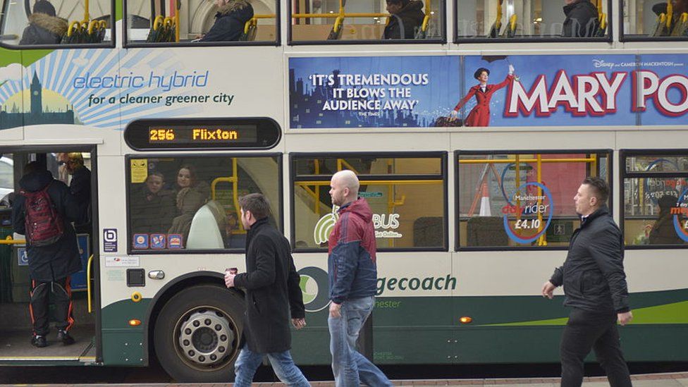 People passing a bus, stationary at a bus stop, in central Manchester