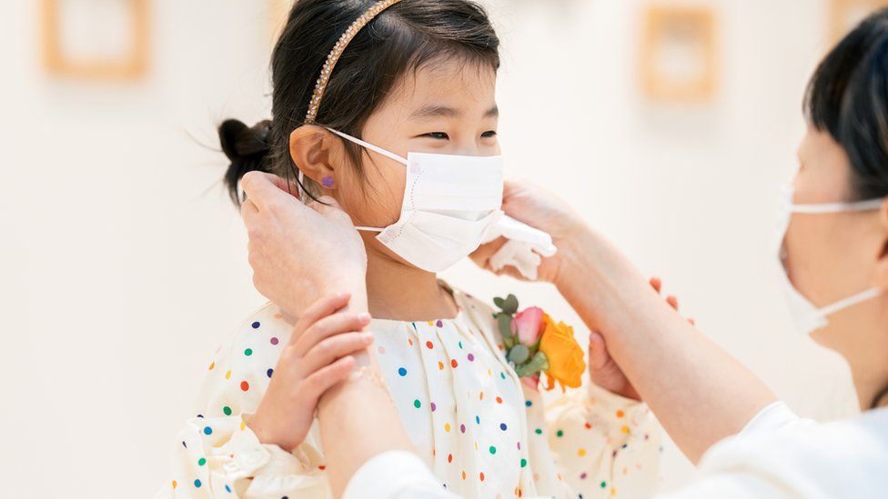 Mother putting protective mask on her young daughter's face.