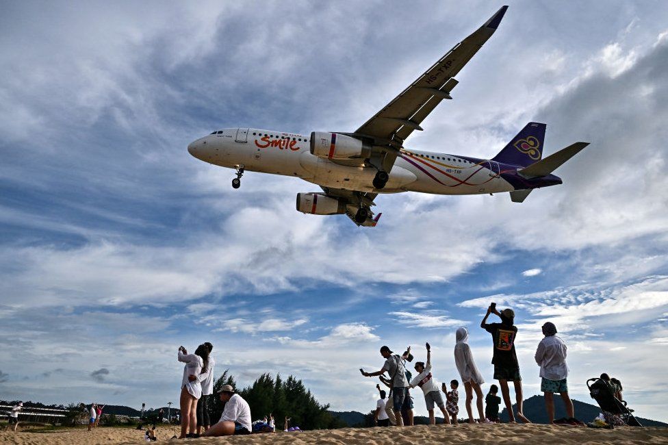 This photograph taken on November 18, 2023, shows tourists posing for pictures on the Mai Khao Beach as an airplane lands at Phuket International Airport in the southern Thai island of Phuket.