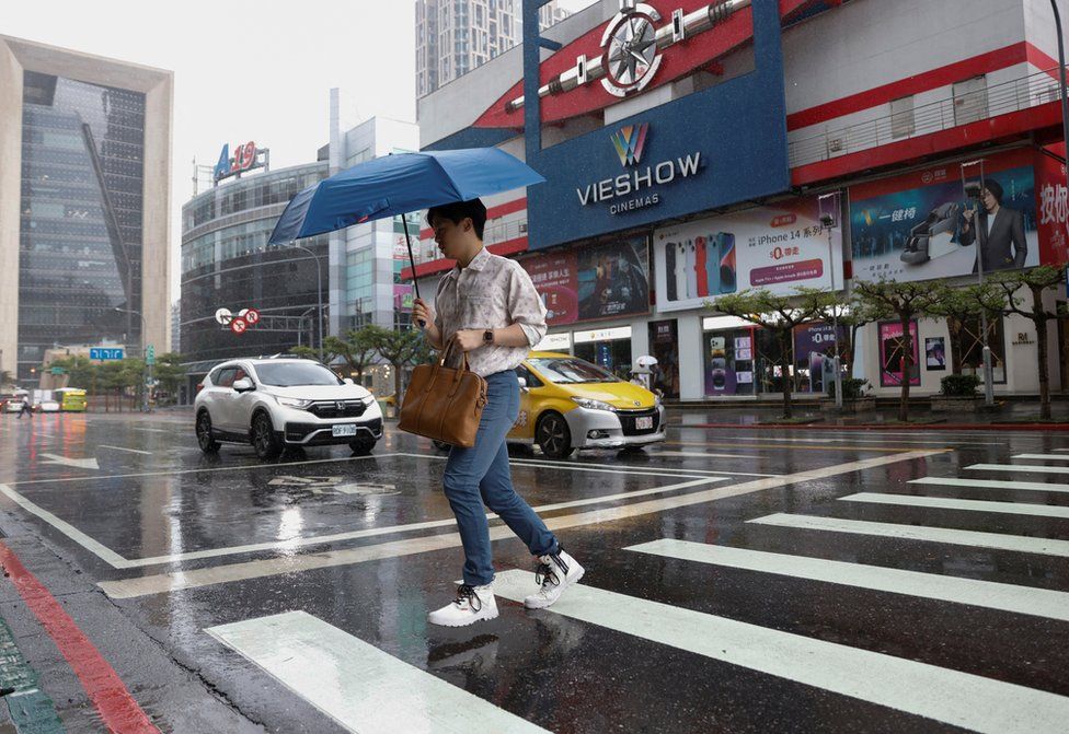 A man crosses the street as it rains at a commercial area where most stores are closed amid warnings of floods and high winds in northern Taiwan due to Typhoon Khanun, in Taipei, Taiwan, August 3, 2023.