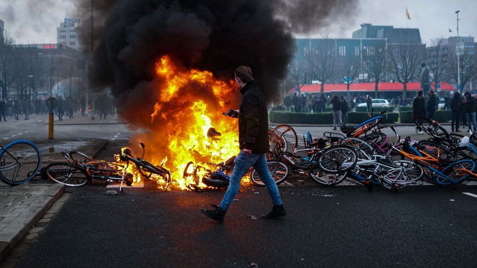 Протестующие кладут велосипеды, чтобы заблокировать улицу, и поджигают во время акции протеста против мер по борьбе с коронавирусом (Covid-19) возле центрального вокзала Эйндховена в Эйндховене
