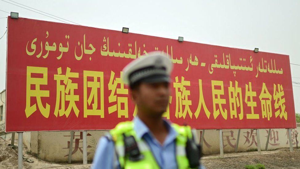A policeman stands in front of a billboard in Kashgar reading 'National unity is the lifeline for people of all ethnic groups', 19 July 2023
