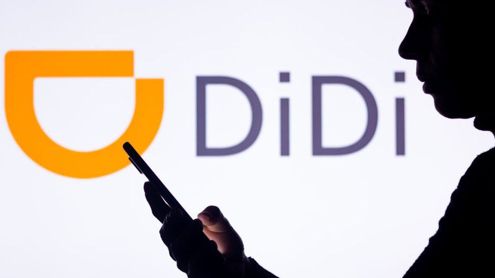 Silhouette of woman holding a smartphone with the Didi Chuxing logo in the background.