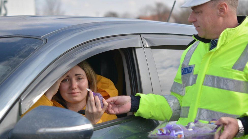 Полицейский протягивает фиолетовые цветы женщине через окно машины