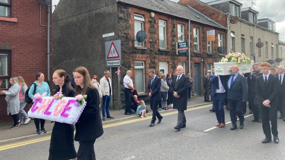 Mourners watch as Chloe Mitchell's coffin is carried along a street to Harryville Presbyterian Church in Ballymena