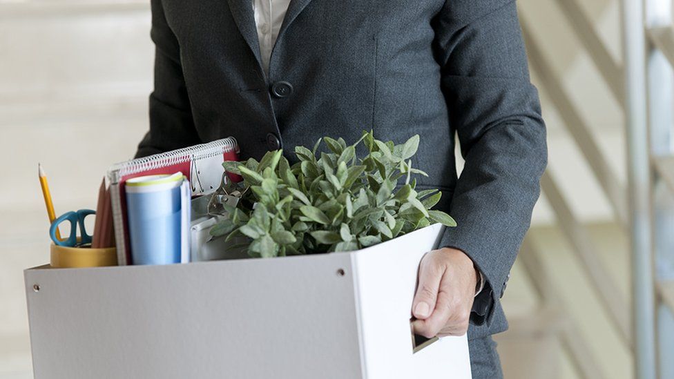 Woman in business suit carrying box out of office, having just been made redundant
