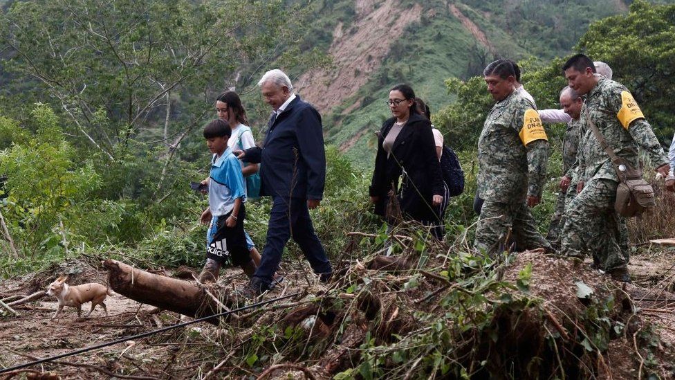 Mexican President Andres Manuel Lopez Obrador (3-L), accompanied by members of his cabinet and other people, walks among debris as they visit the El Kilometro 42 community, near Acapulco, Guerrero State, Mexico, after the passage of Hurricane Otis, on October 25, 2023.