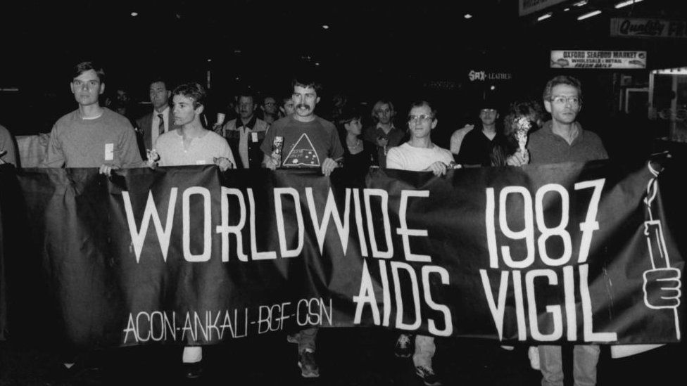 Five men march along a street in Sydney with a banner saying: "Worldwide 1987 Aids vigil."