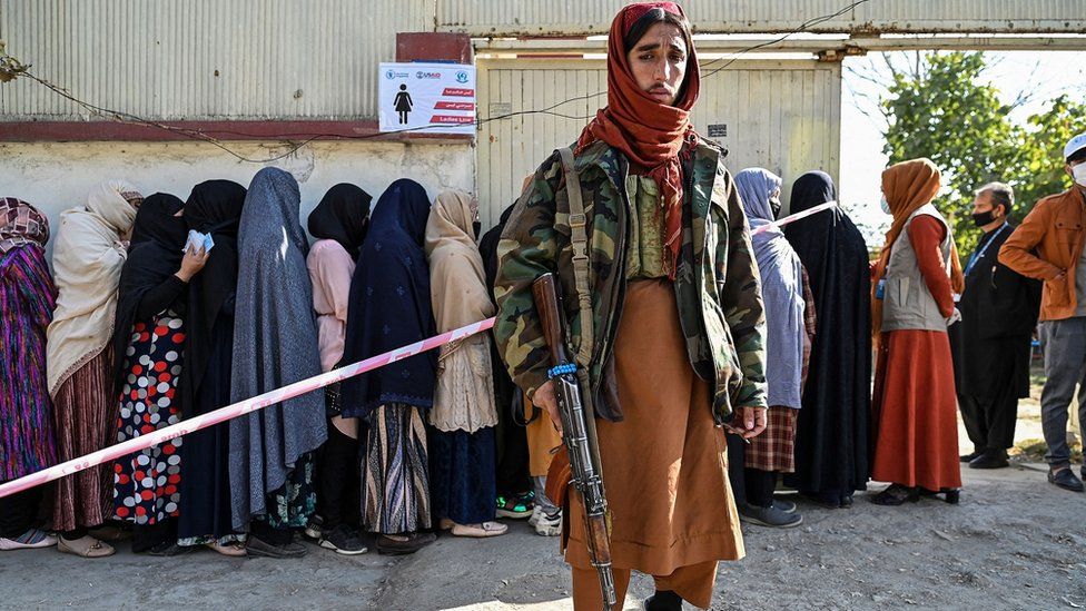 Боец Талибана стоит на страже женщин, стоящих в очереди во время раздачи продовольствия Всемирной продовольственной программы в Кабуле