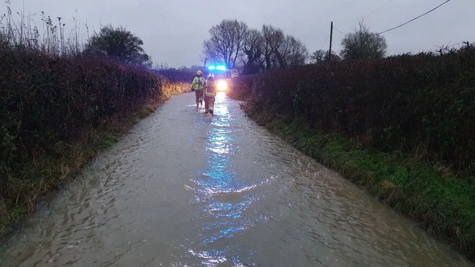 Rescue crews wading through a flooded country road