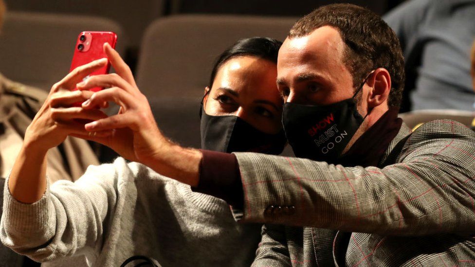 Two people wearing masks take a selfie using an iPhone