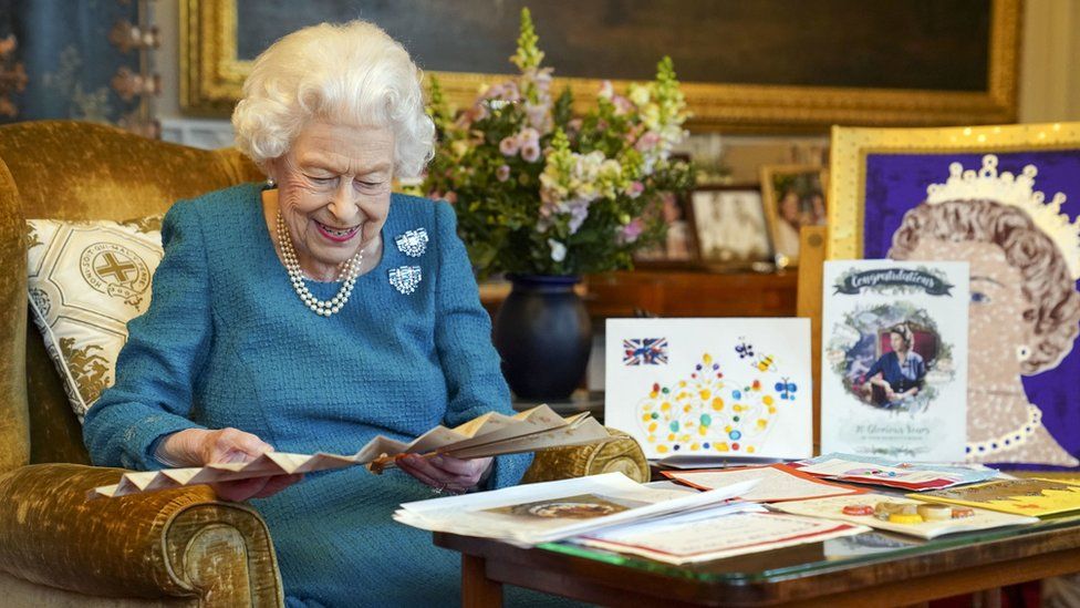 Королева смотрит на веер, окруженный памятными вещами с ее юбилеев