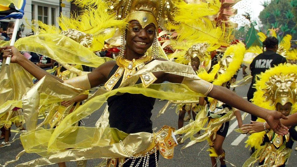 A woman dancing in a yellow and gold costume at the Notting Hill Carnival