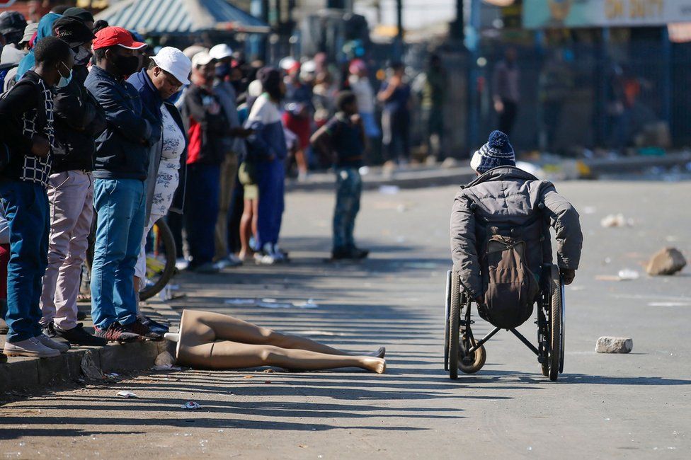 People look at a man in a wheelchair as he moves past the looted and vandalised Lotsoho Mall in Katlehong township, East of Johannesburg, on 12 July 2021