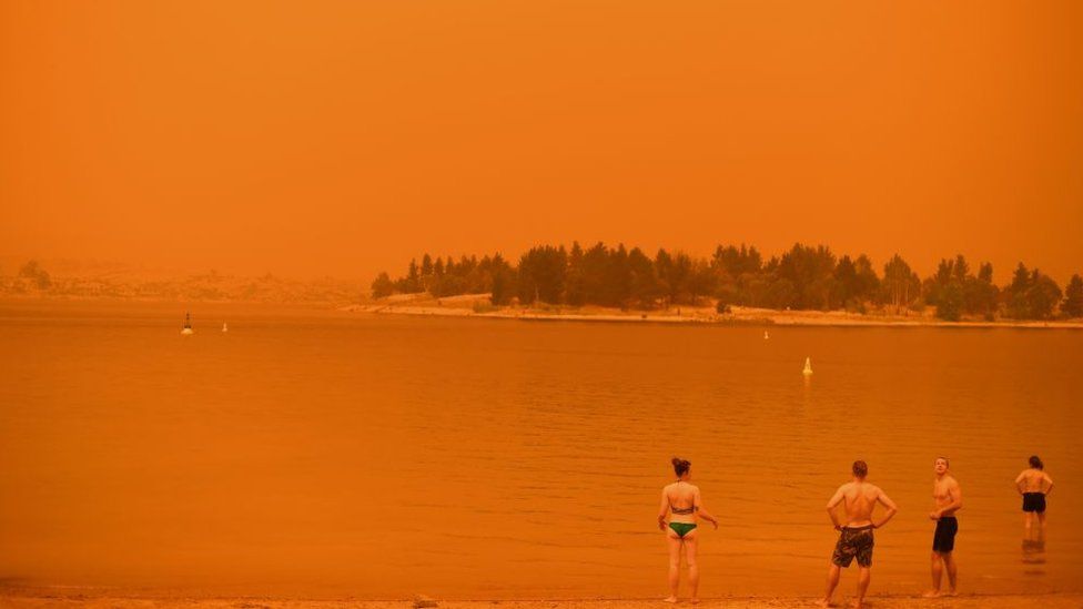 Swimmers stand near the water under a red sky at Jindabyne in New South Wales on 4 January